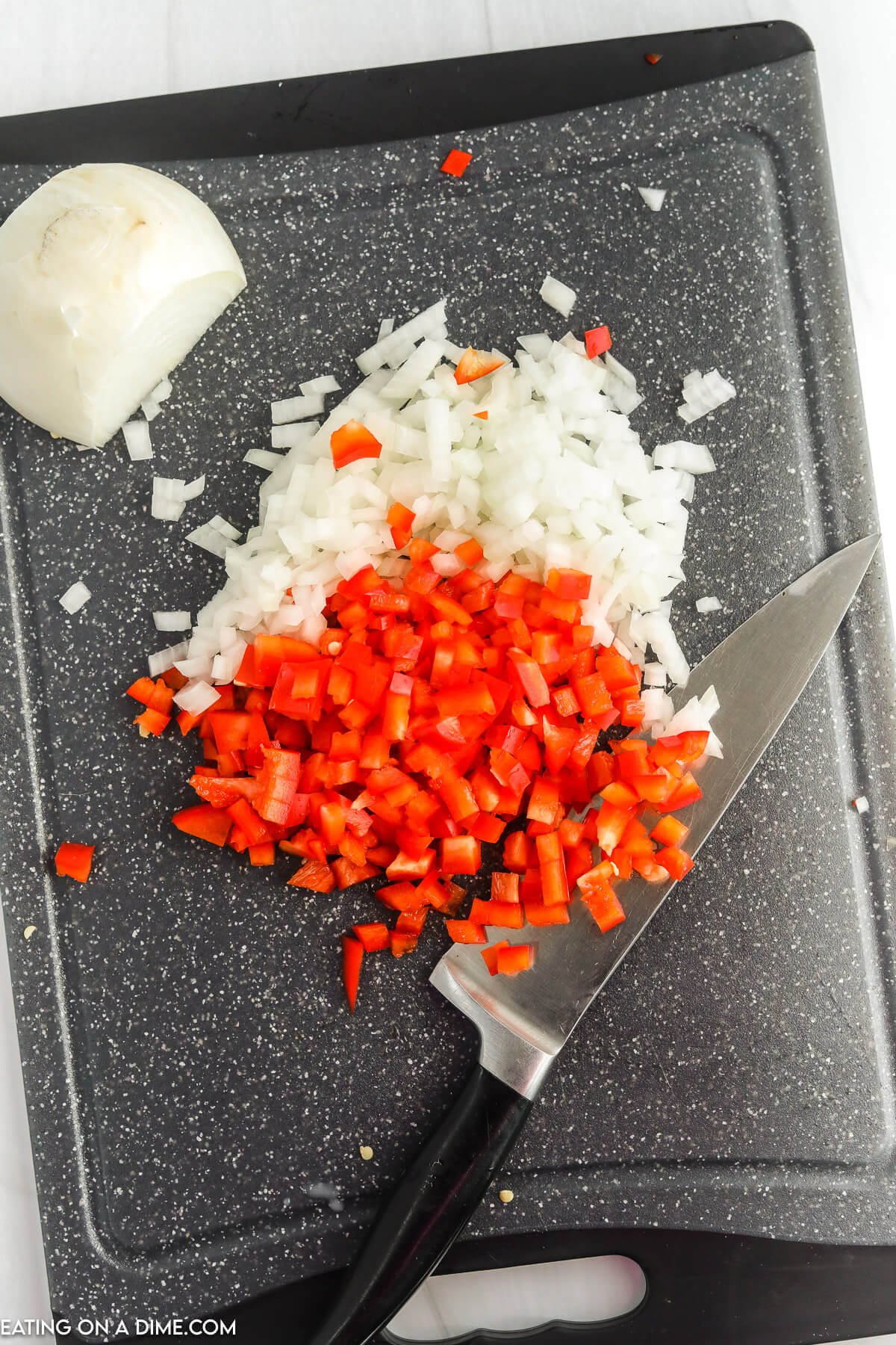 Chopping the red bell peppers and onions on a cutting board with a knife
