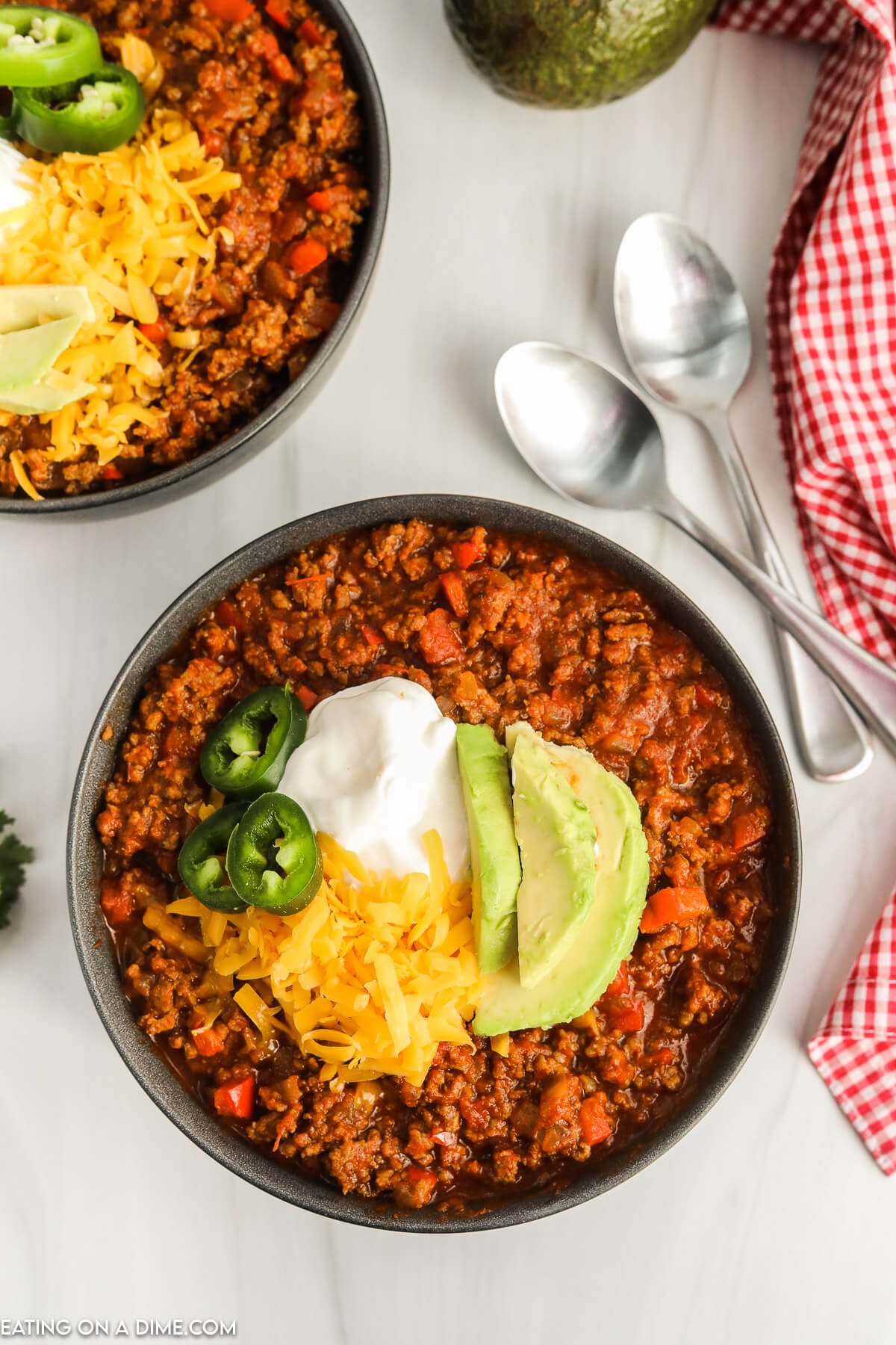 A bowl of chili topped with shredded cheese slice jalapenos sour cream and slice avocados