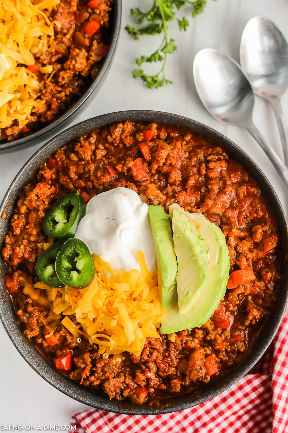 A bowl of chili topped with shredded cheese slice jalapenos sour cream and slice avocados