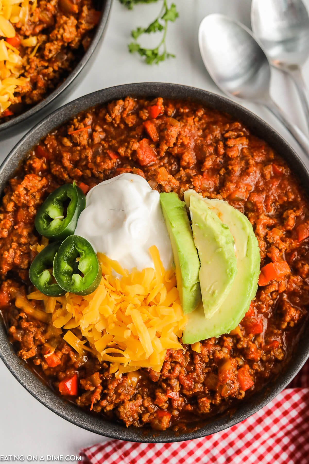 A bowl of chili topped with shredded cheese slice jalapenos sour cream and slice avocados