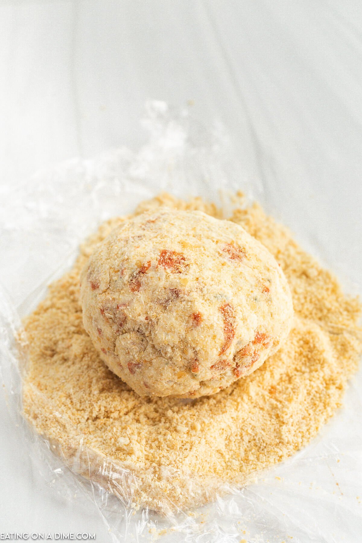 Rolling the cheese ball into the crushed crackers on plastic wrap