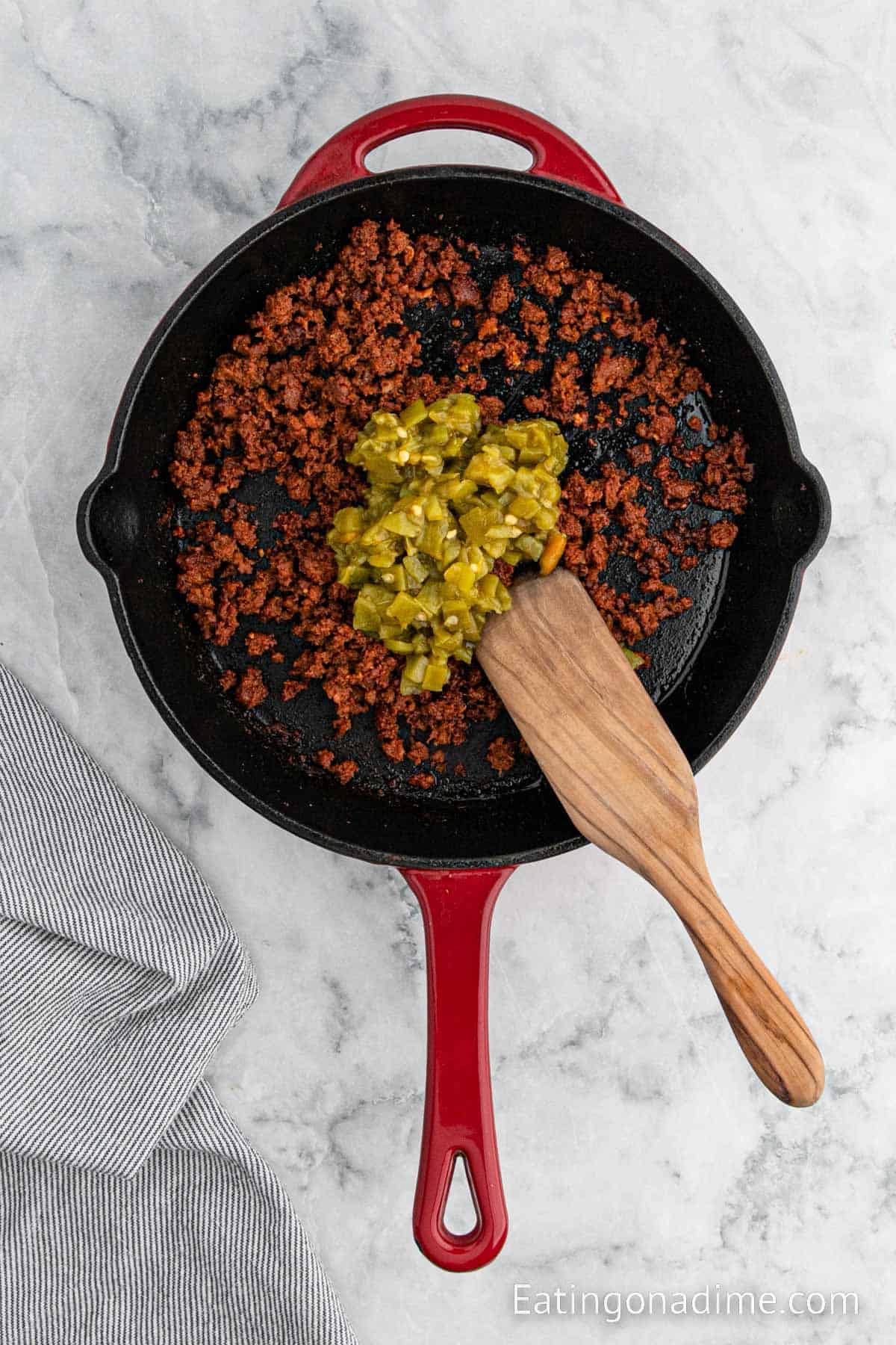 Stirring in green chiles into the ground chorizo in a cast iron skillet with a wooden spoon