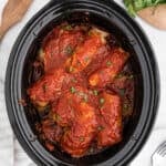 A slow cooker filled with savory slow cooker cabbage rolls, topped with tomato sauce and sprinkled with chopped parsley, ready to serve on a countertop.
