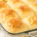 A close-up of golden brown, freshly baked 30 minute dinner rolls in a glass baking dish, showing their shiny, soft, and fluffy tops.
