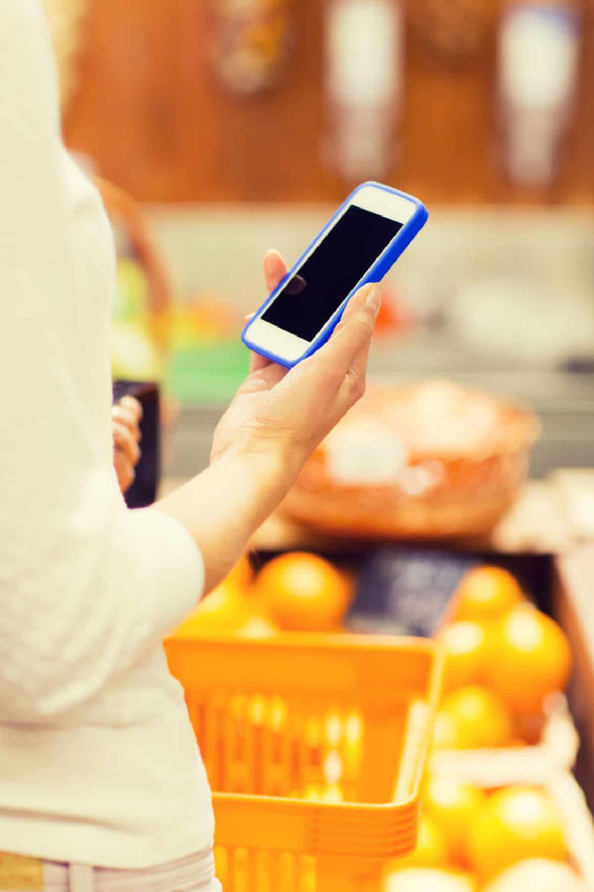 A lady looking at her smart phone while grocery shopping 