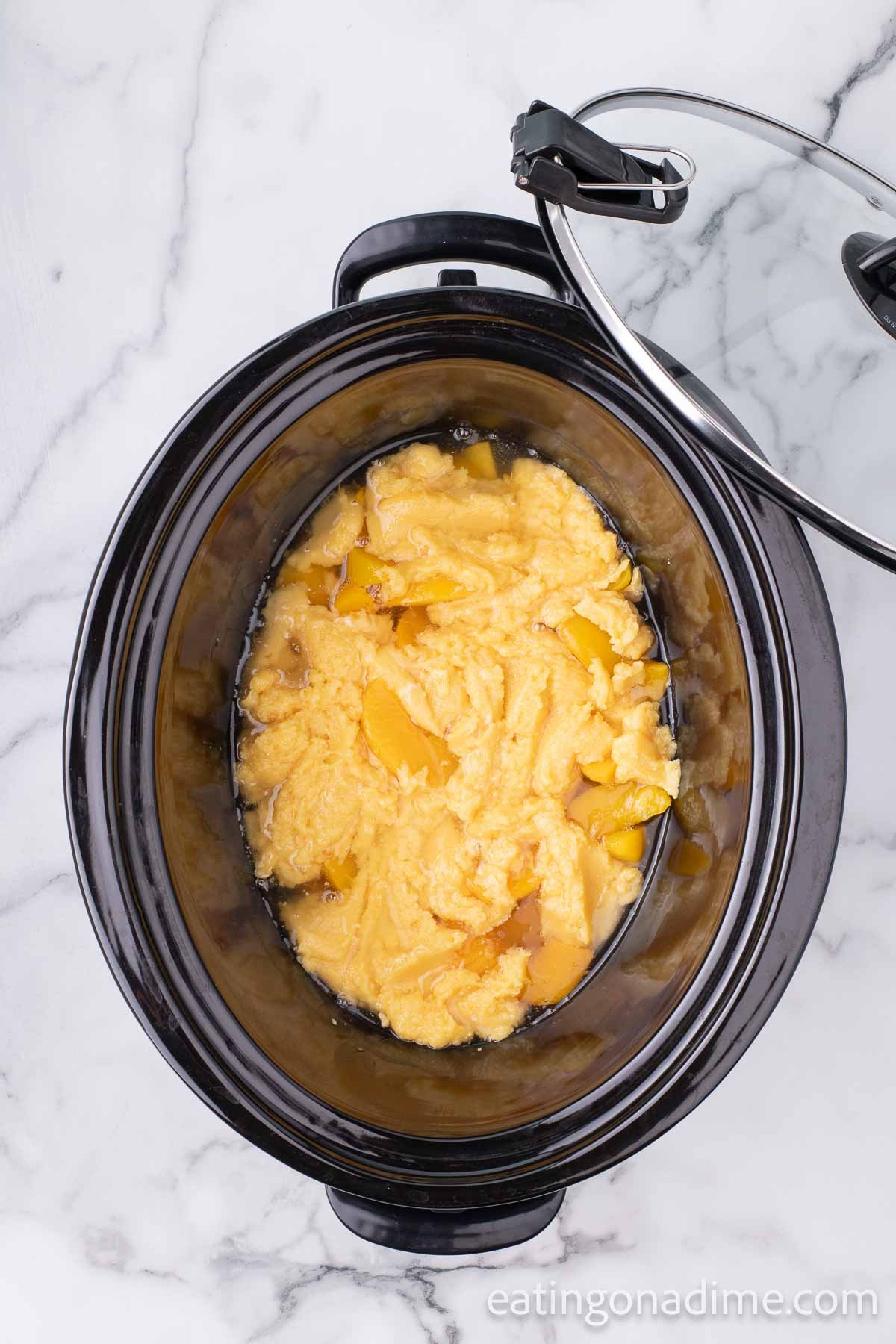 Topping the peaches in the slow cooker with the cake mix mixture