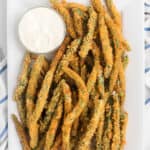 A platter of crispy breaded green bean fries, made with an easy fried green beans recipe, is served with a small bowl of creamy dipping sauce on the side.