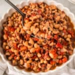 A close-up of a bowl filled with Instant Pot Black Eyed Peas mixed with diced tomatoes and onions. A spoon is lifting a serving from the bowl.