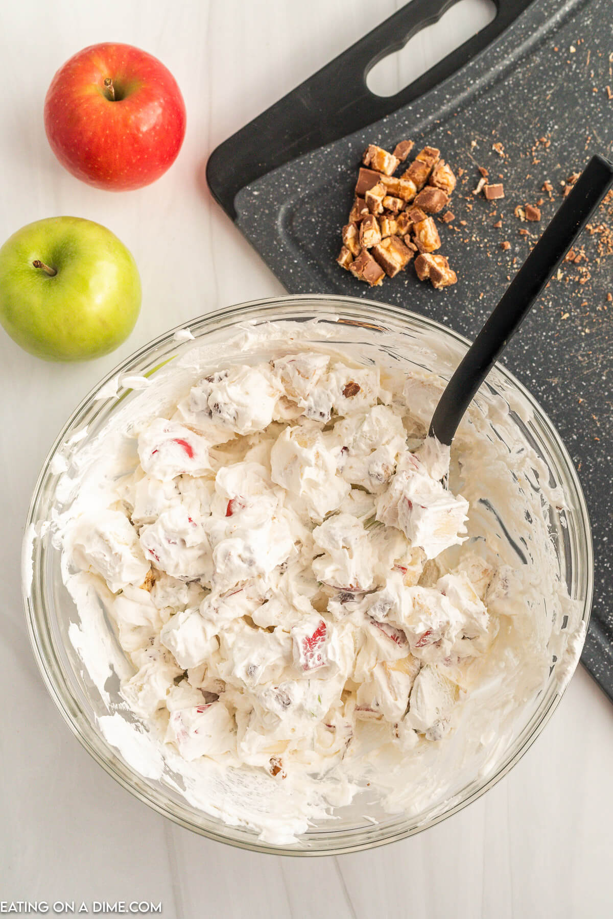 Adding the chopped apples and snickers to the whipped topping in a bowl