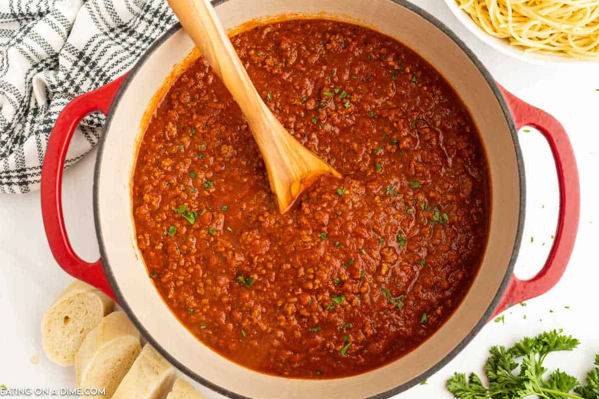 Bolognese Sauce in a large Dutch Oven with a wooden spoon.