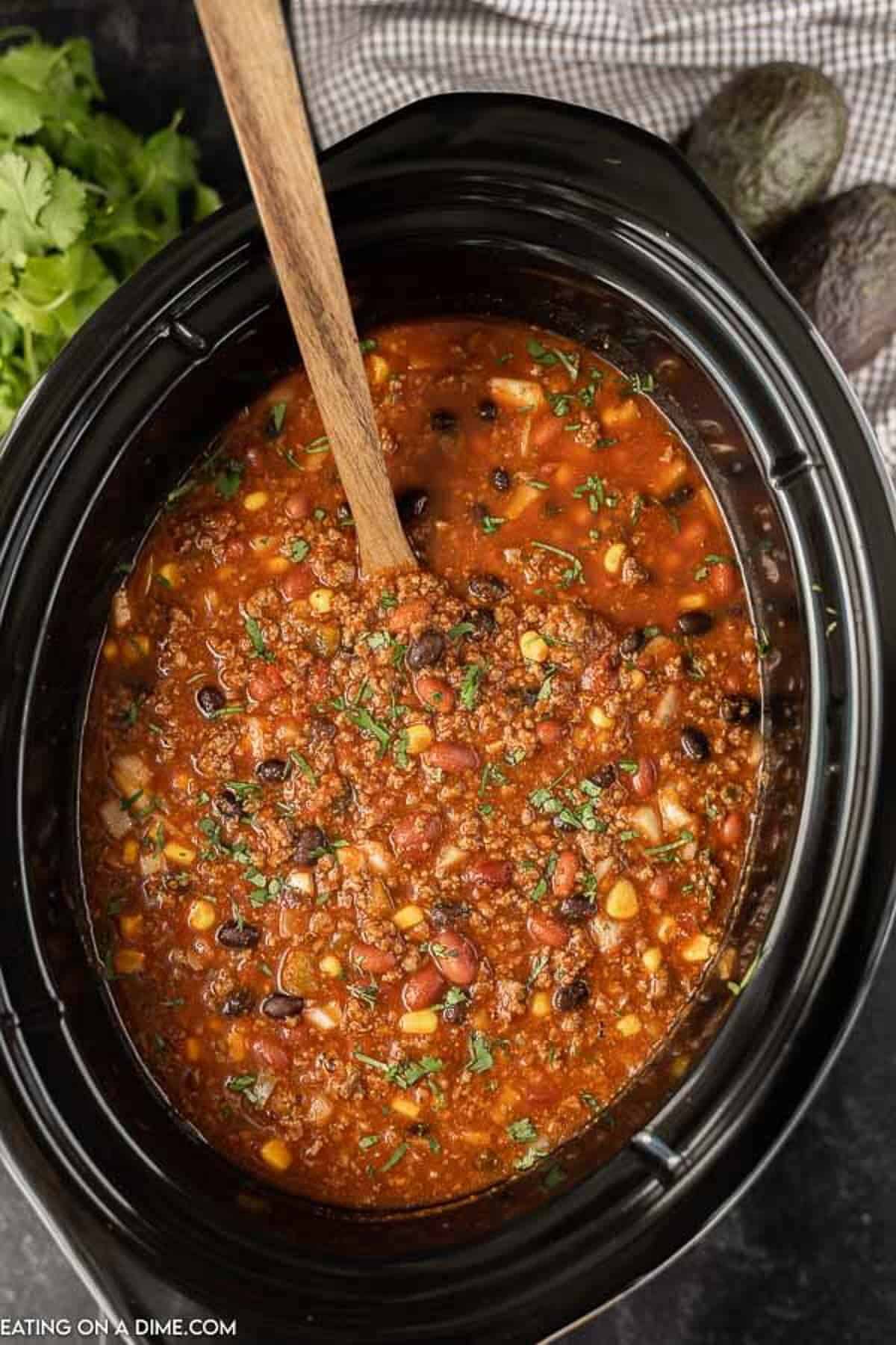 Taco chili cooked in a crock pot topped with fresh diced cilantro with a serving spoon in the taco chili.  