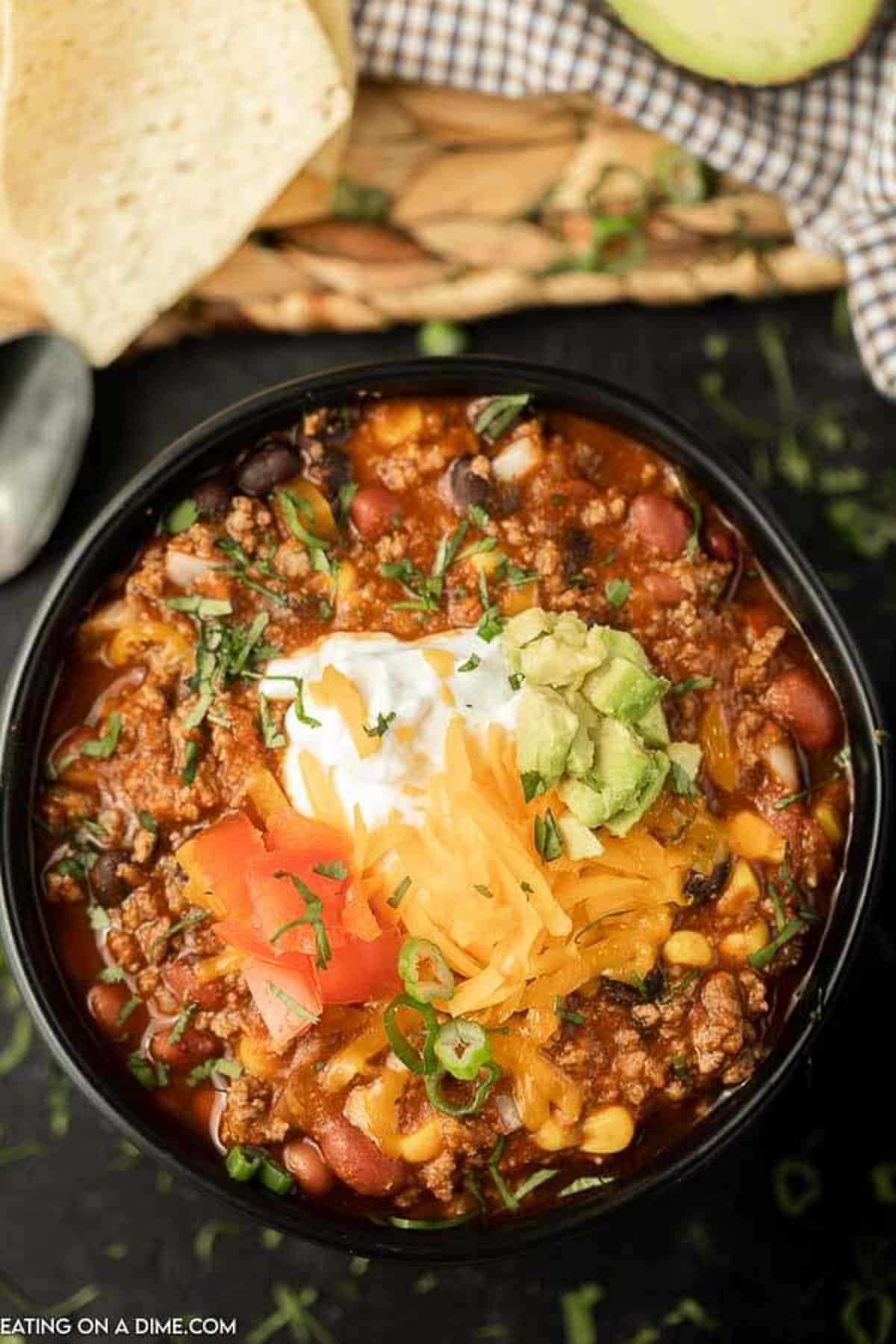 A bowl of taco chili topped with sour cream, shredded cheese, diced avocado, diced tomatoes and chopped cilantro.  
