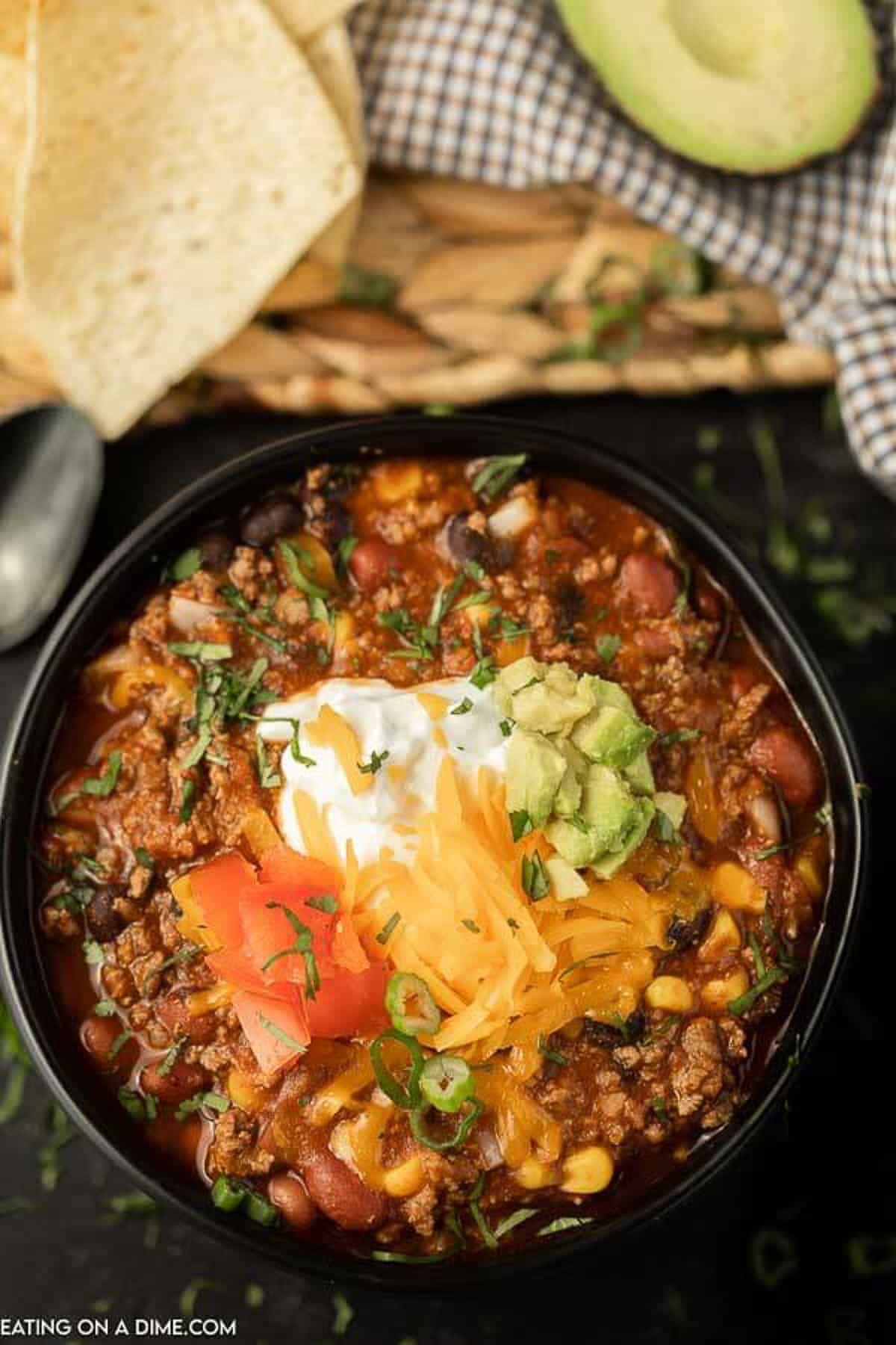 A bowl of taco chili topped with sour cream, shredded cheese, diced avocado, diced tomatoes and chopped cilantro.  