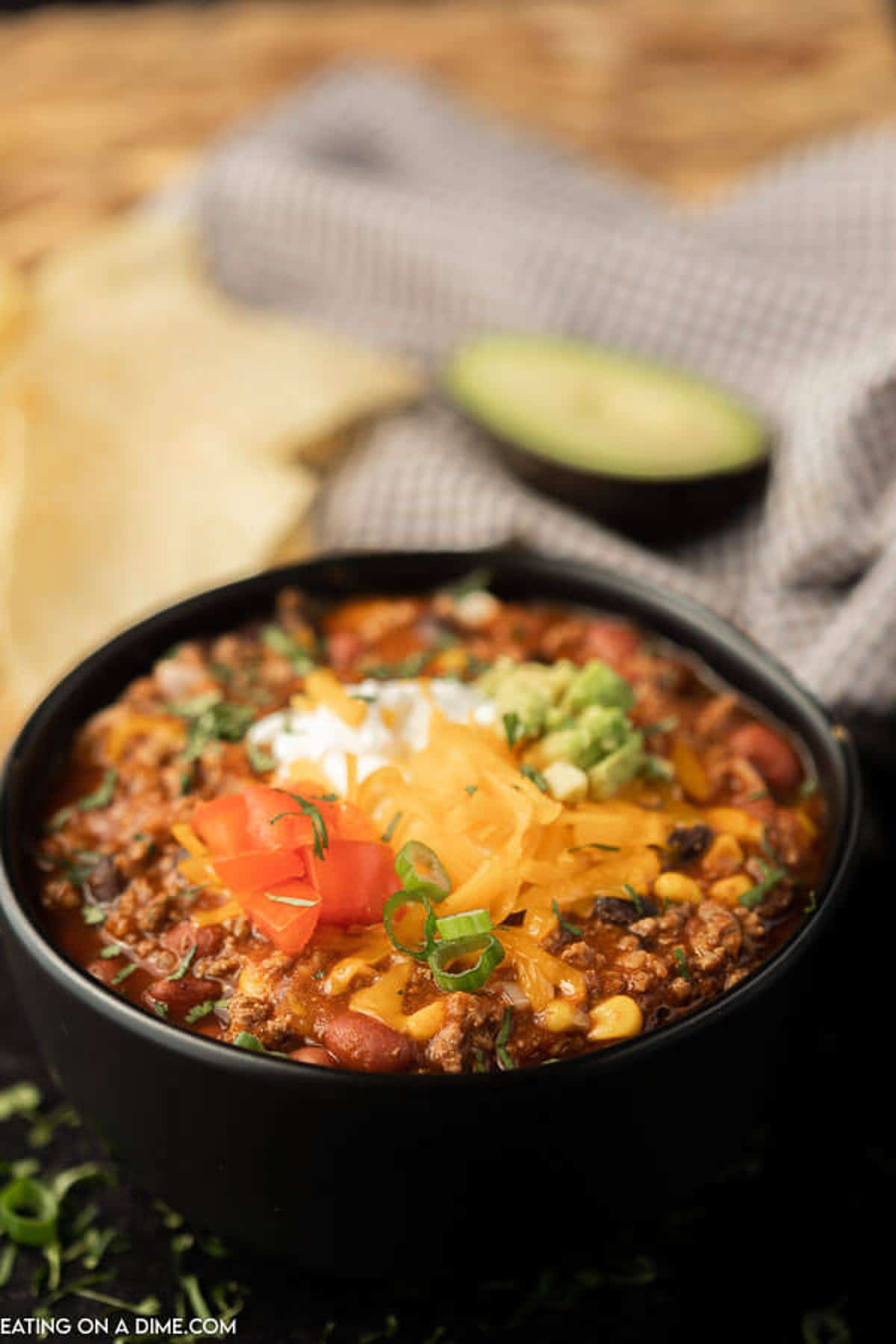A bowl of taco chili topped with sour cream, shredded cheese, diced avocado, diced tomatoes and chopped cilantro.  