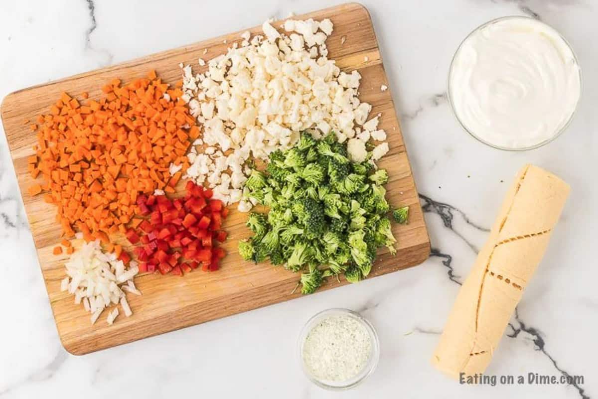 ingredients for crescent roll veggie pizza: carrots, onion, bell peppers, cauliflower, broccoli, ranch, crescent rolls