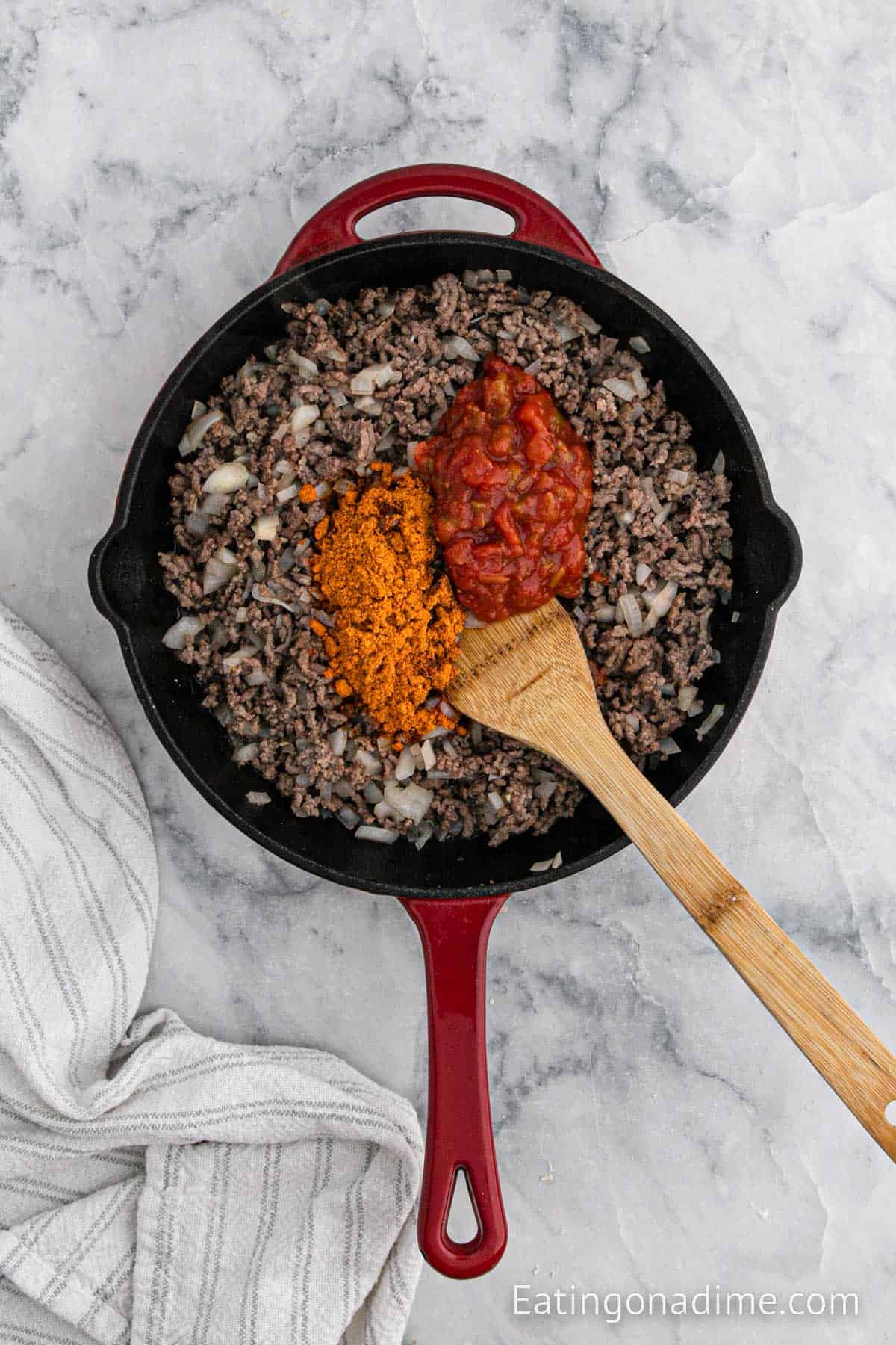 Adding in the salsa and taco seasoning to the ground beef mixture with a wooden spoon