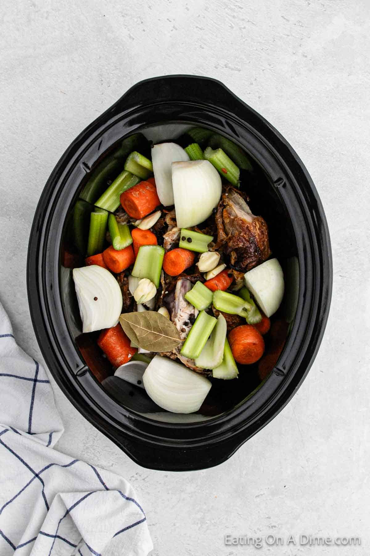 Adding the veggies to the slow cooker with carcass
