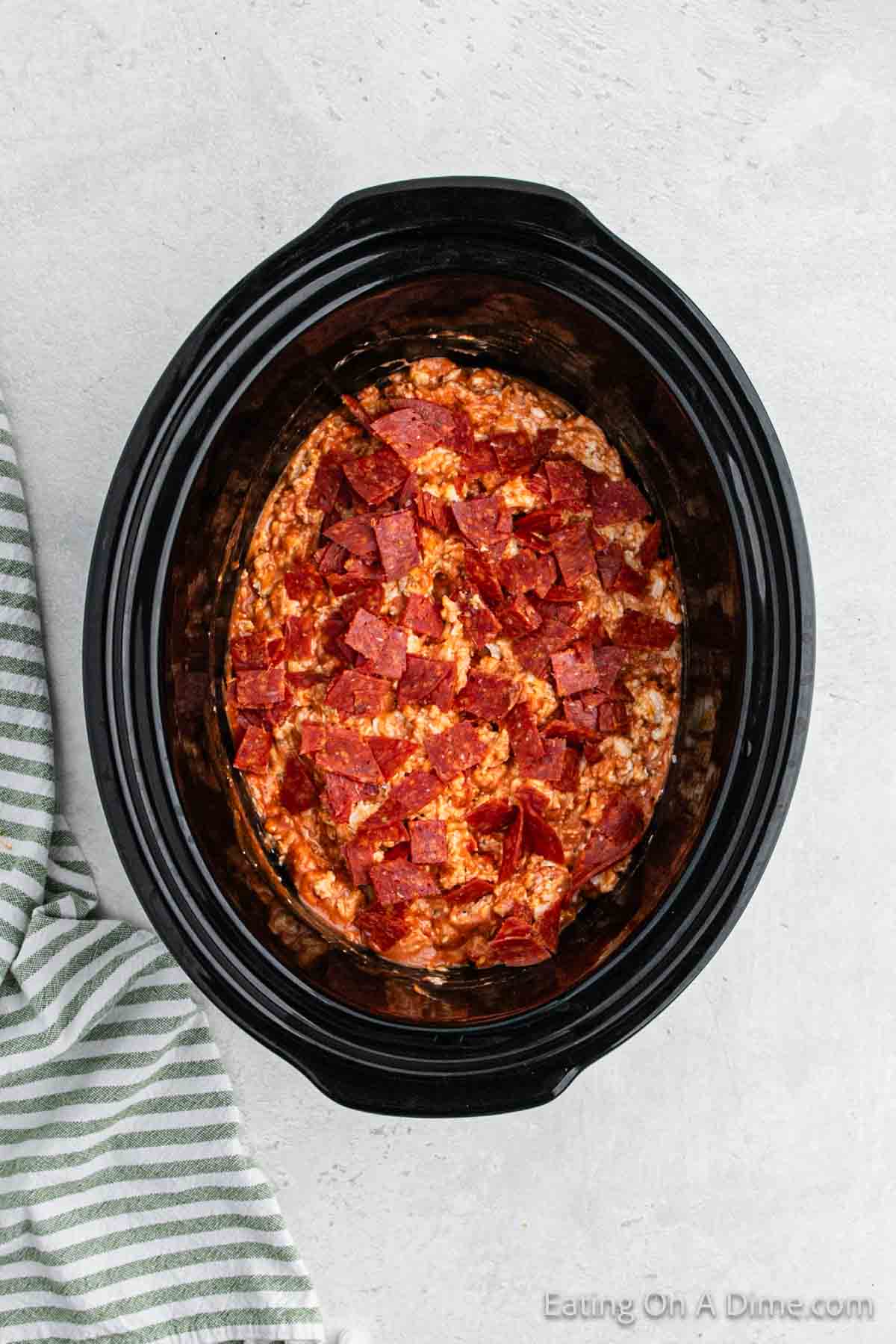 Adding chopped pepperoni to the mixture in the slow cooker