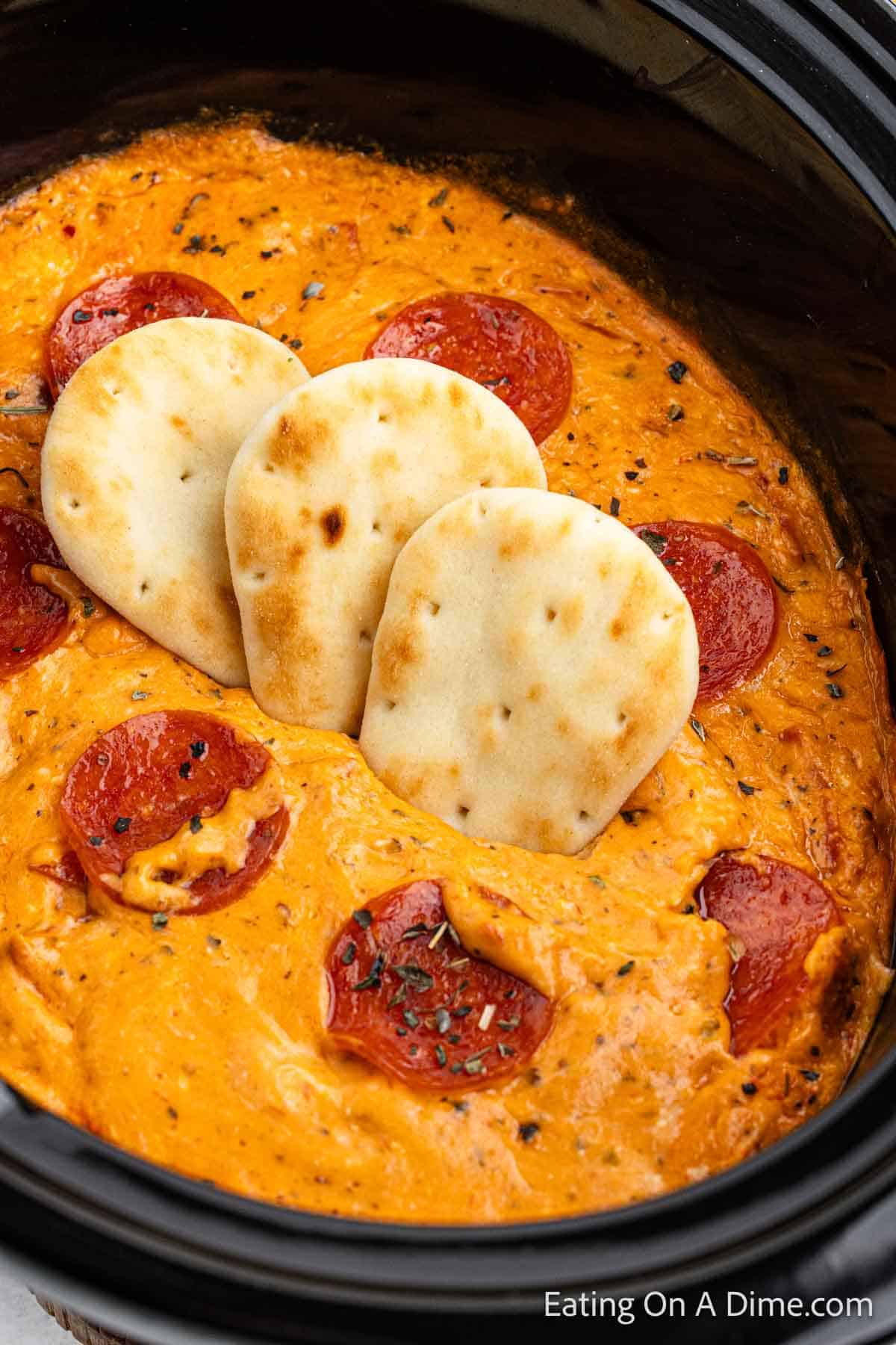 Pizza dip in the slow cooker topped with pepperonis and pita bread