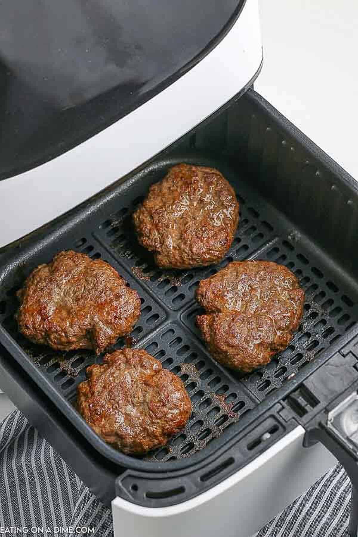 4 hamburger patties being cooked in an air fryer basket.  