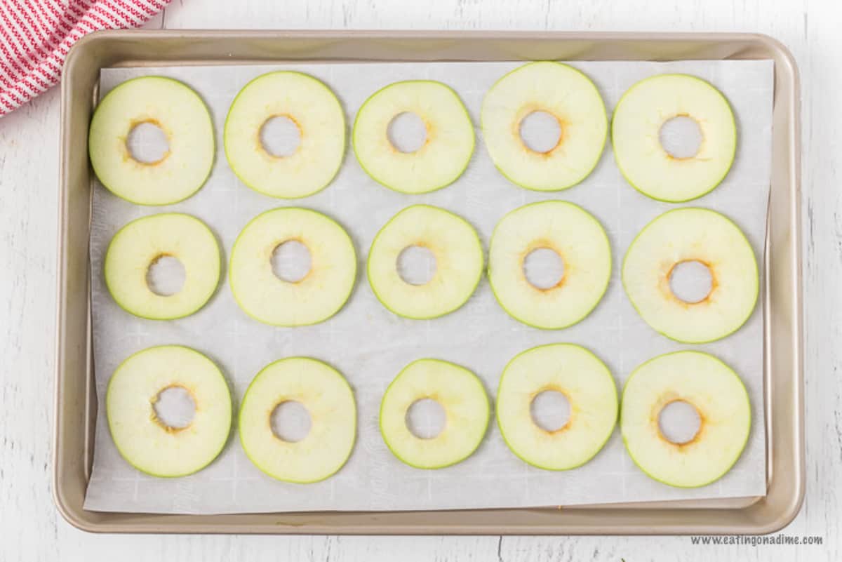 The apple slices laid out on a baking sheet topped with parchment paper.  