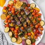 Greek chicken kabobs with roasted zucchini, squash and tomatoes on a plate.