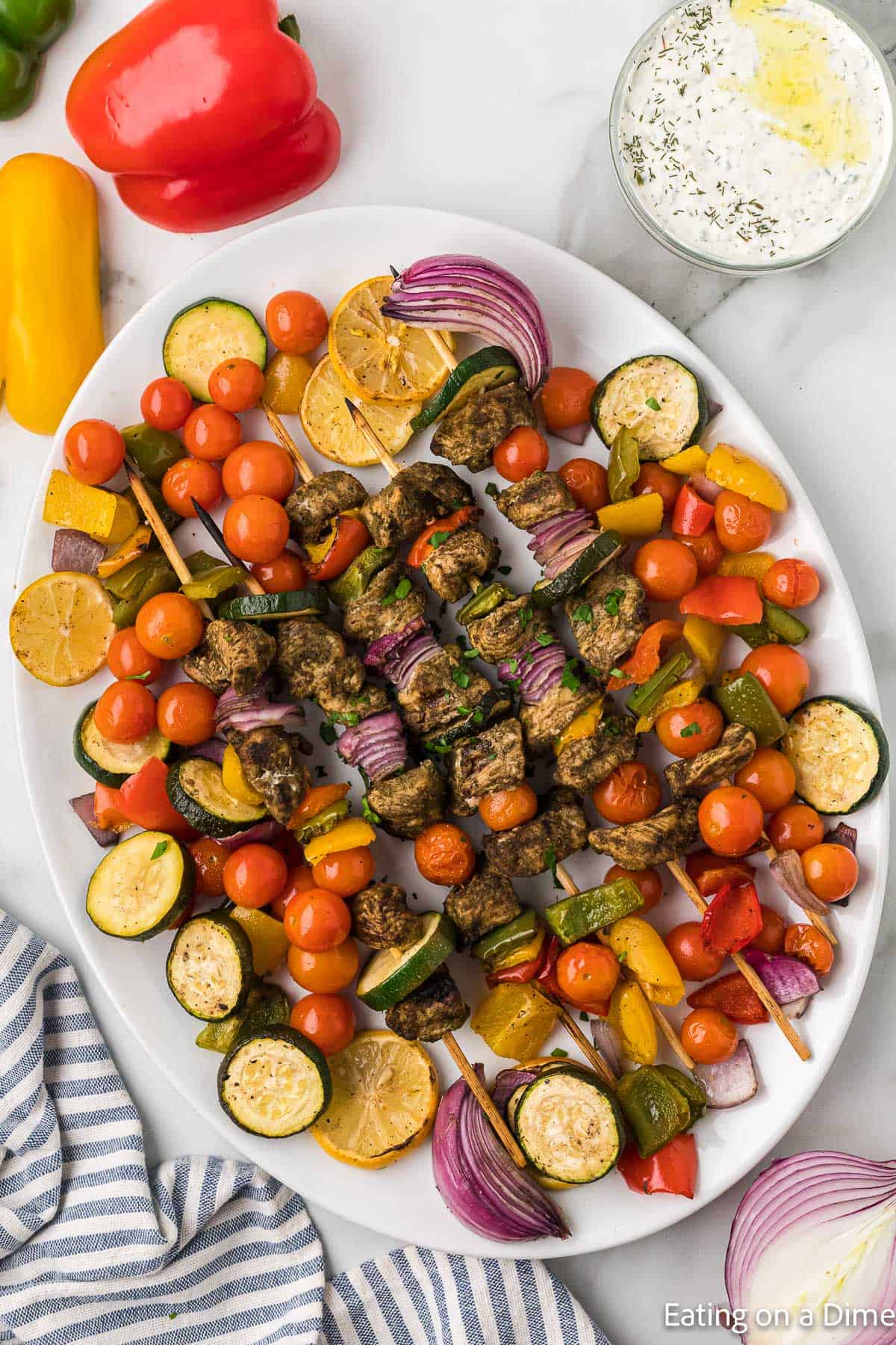 Greek Chicken Kabobs on a platter with cherry tomatoes, red onions, and zucchini
