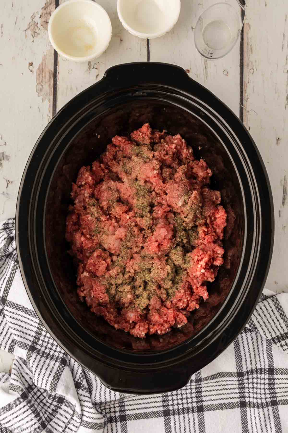 Placing the raw ground beef in the slow cooker with the seasoning