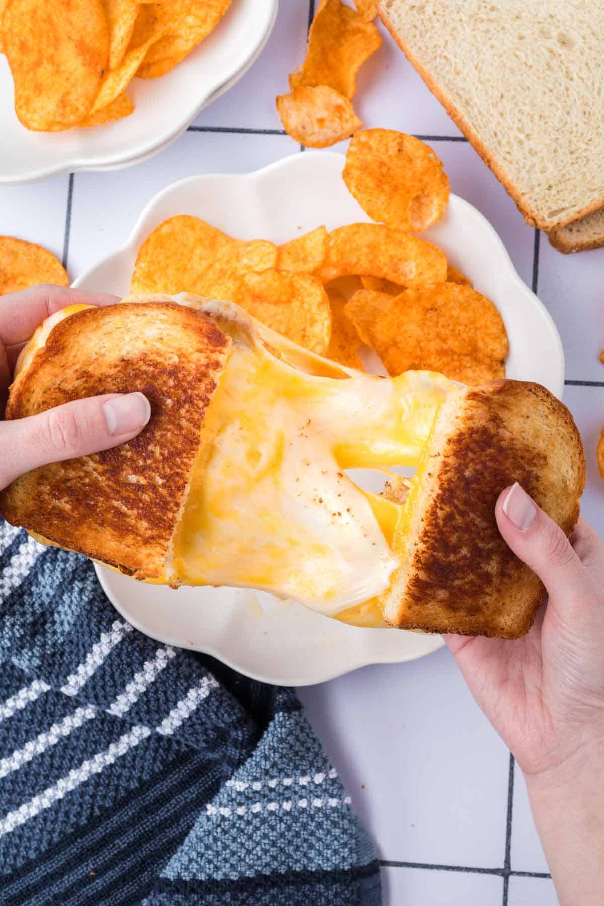 Grilled Cheese Sandwich being pulled apart with melty cheese in the center with a side of potato chips