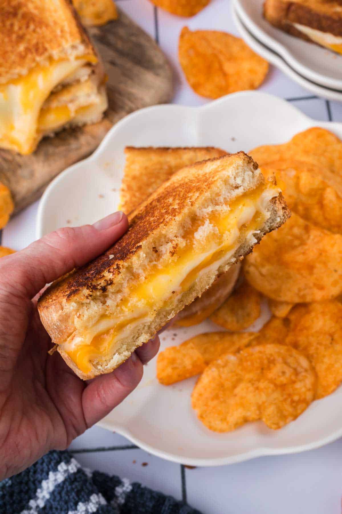 Close up image of half of grilled cheese being held with a plate of chips in the background