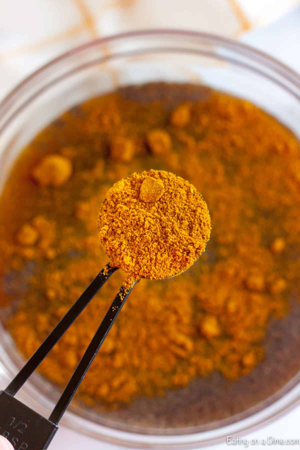 Table spoon of curry powder being added to the bowl of seasoning