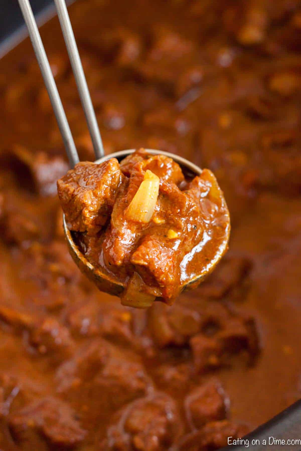 Cooked beef curry in the slow cooker with a serving on the ladle