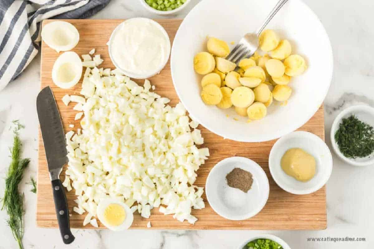 Chopping the egg white and mashing the egg yolks in a bowl with small bowls of mustard, mayo and spices.