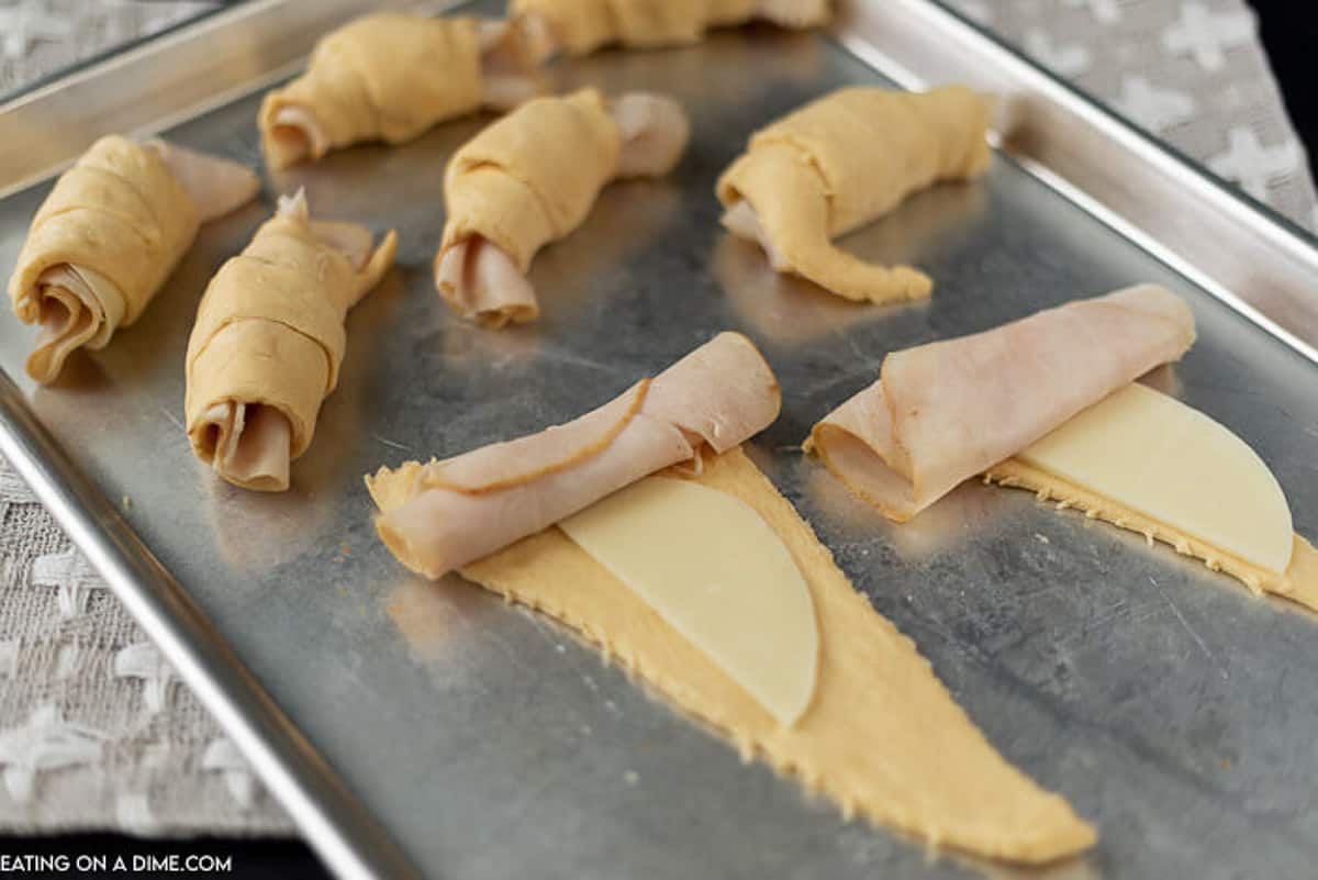 The crescent rolls rolled out on a baking sheet with deli turkey and cheese layered on top.  