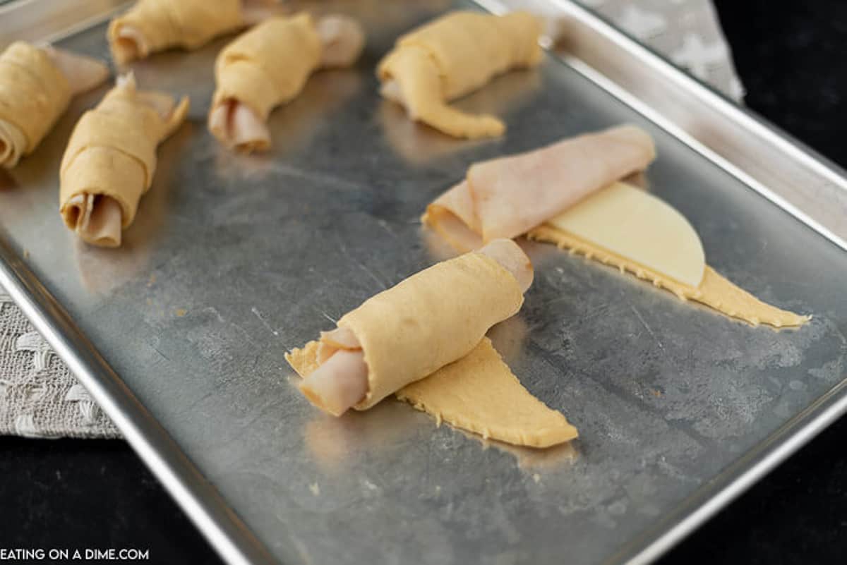 The crescent rolls being wrapped around the turkey and cheese to make the turkey roll-ups.  