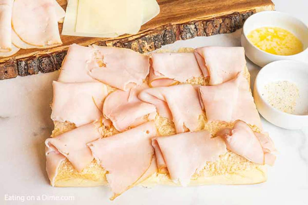 Bottom rolls topped with deli turkey and bowls of melted butter and garlic salt