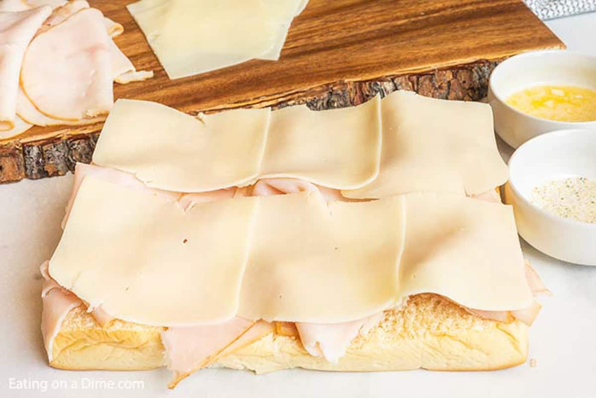 Bottom rolls topped with deli turkey, slices of mozzarella cheese with bowls of melted butter and garlic salt on the side