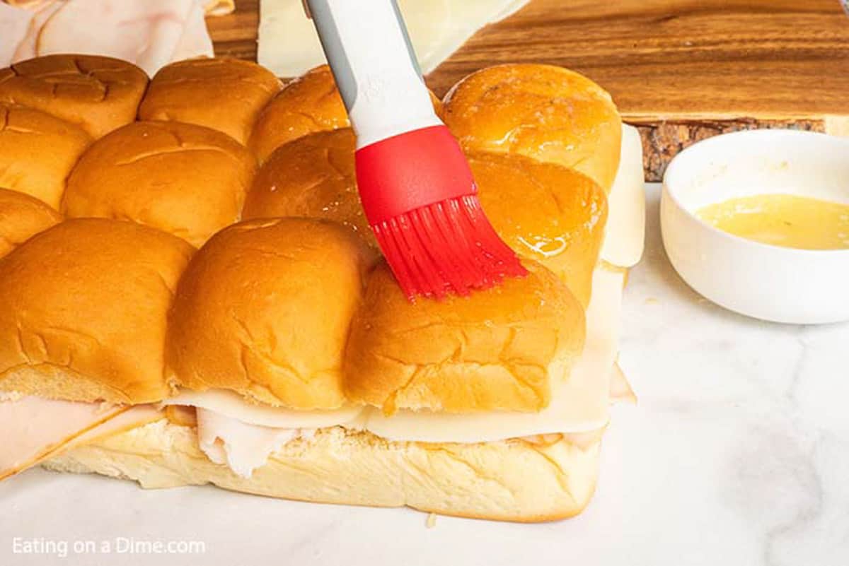 Brushing the melted butter over the tops of the rolls with deli turkey and slice cheese