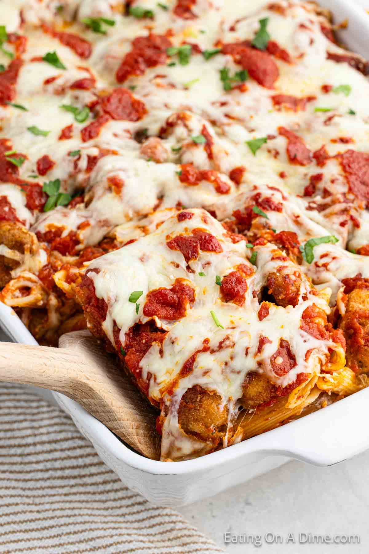 Close up image of chicken parmesan pasta in casserole dish with a serving on a wooden spoon