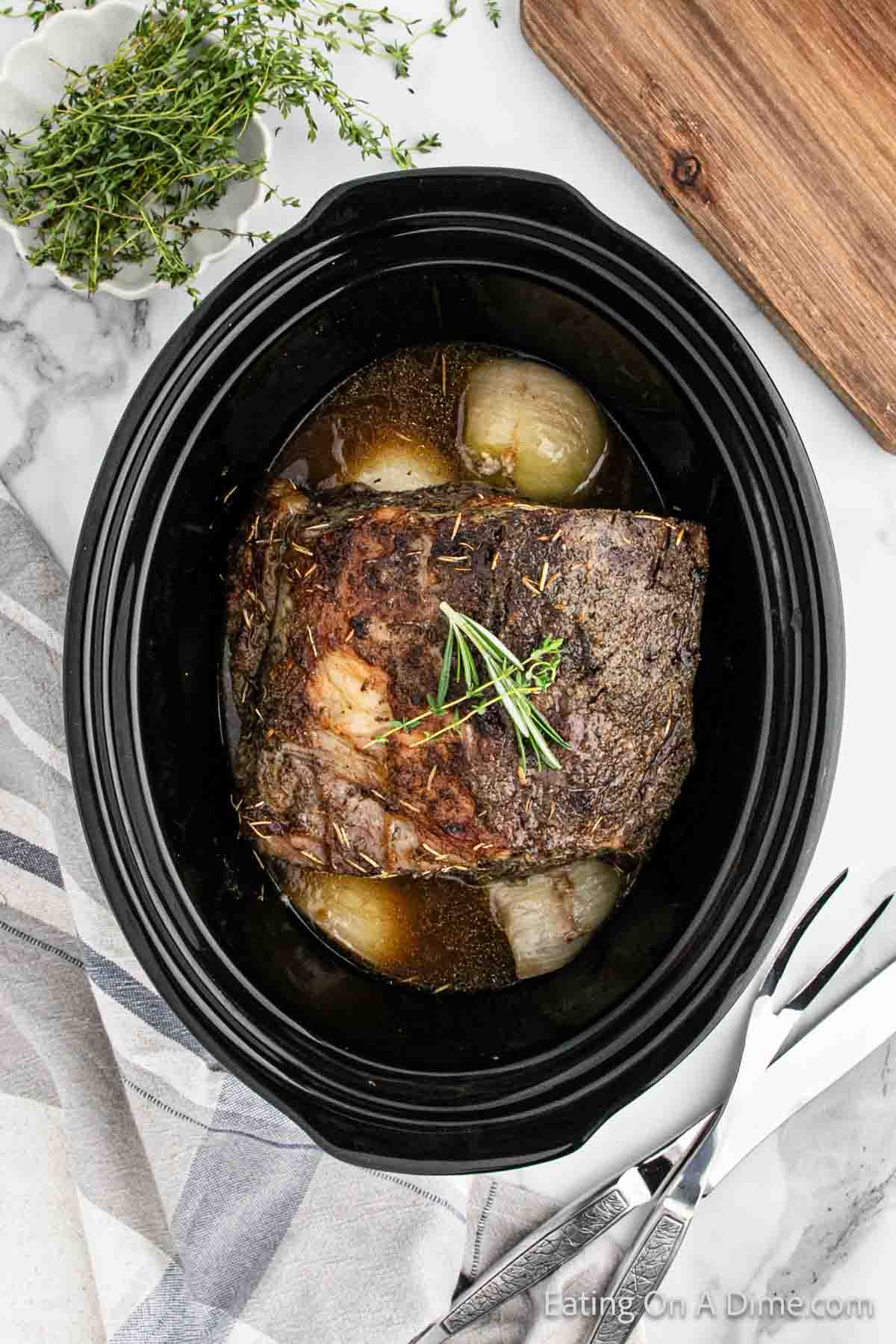 Cooked prime rib in the slow cooker topped with fresh herbs