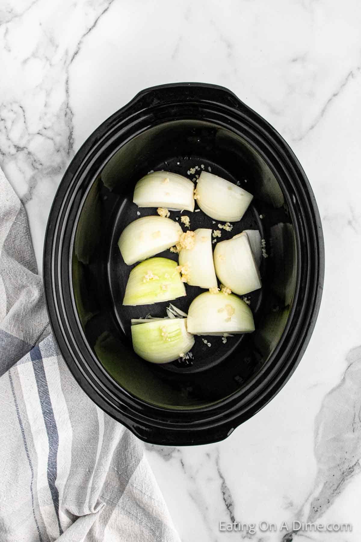 Placing the onions quarters and garlic in the slow cooker