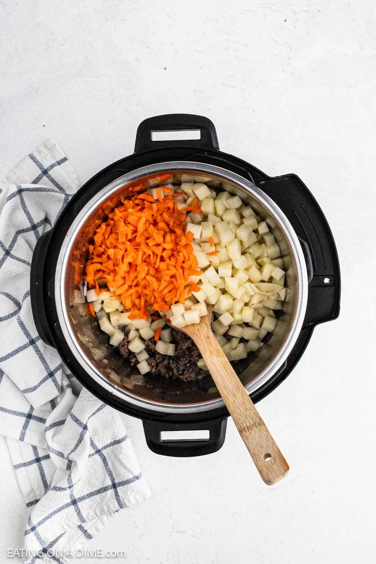 Shredded carrots and potatoes added to the instant pot with the ground beef.