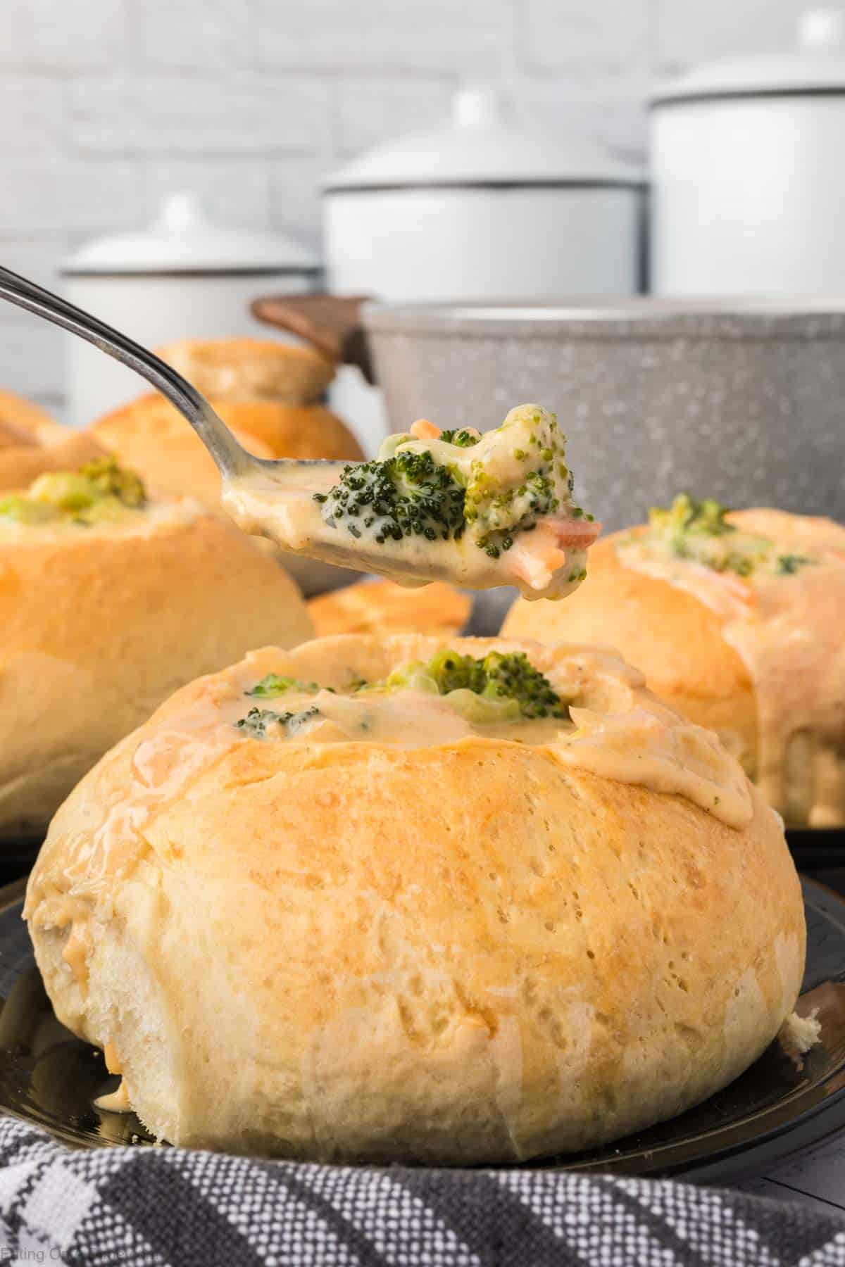 Close up image of bread bowls with a serving of broccoli cheese soup in a spoon