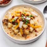 A serving of cheeseburger soup in a bowl topped with shredded cheese and green onions.