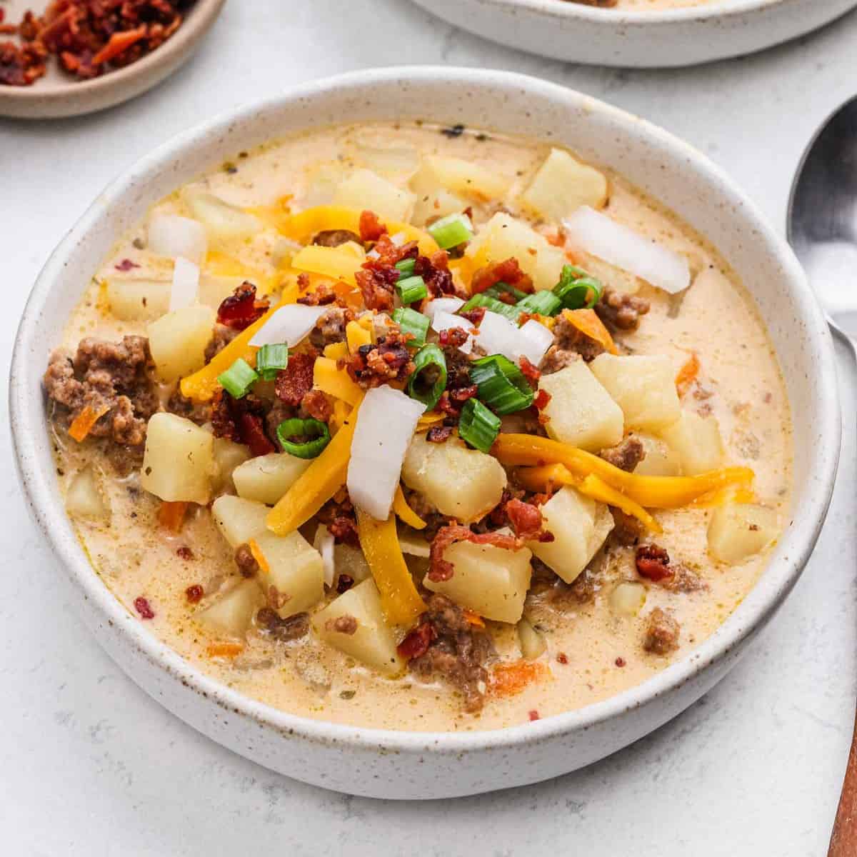 A serving of cheeseburger soup in a bowl topped with shredded cheese and green onions.