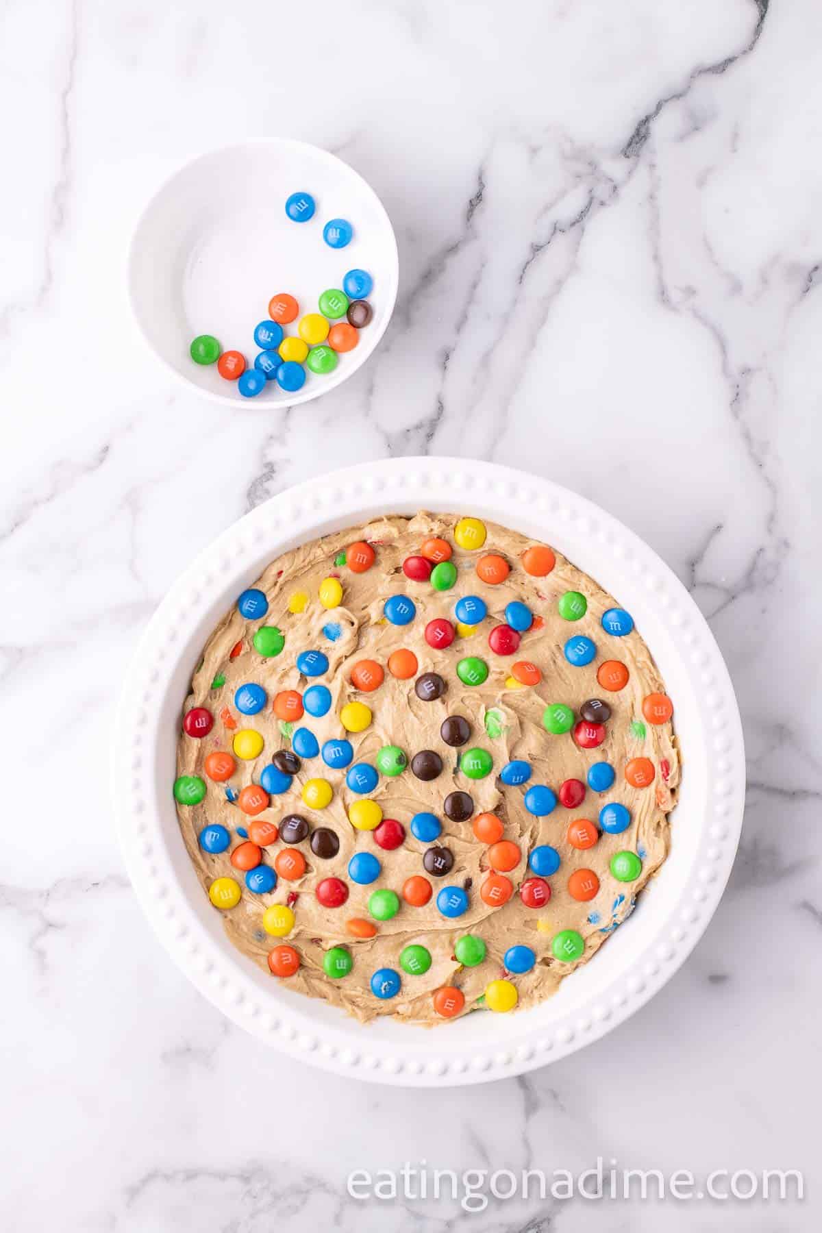 Pressing the cookie batter into the prepared pan and topped with M&M