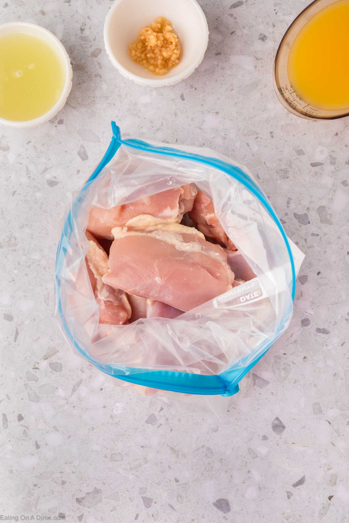 Chicken thighs placed in a ziplock bag with bowls of lime juice, minced garlic and orange juice