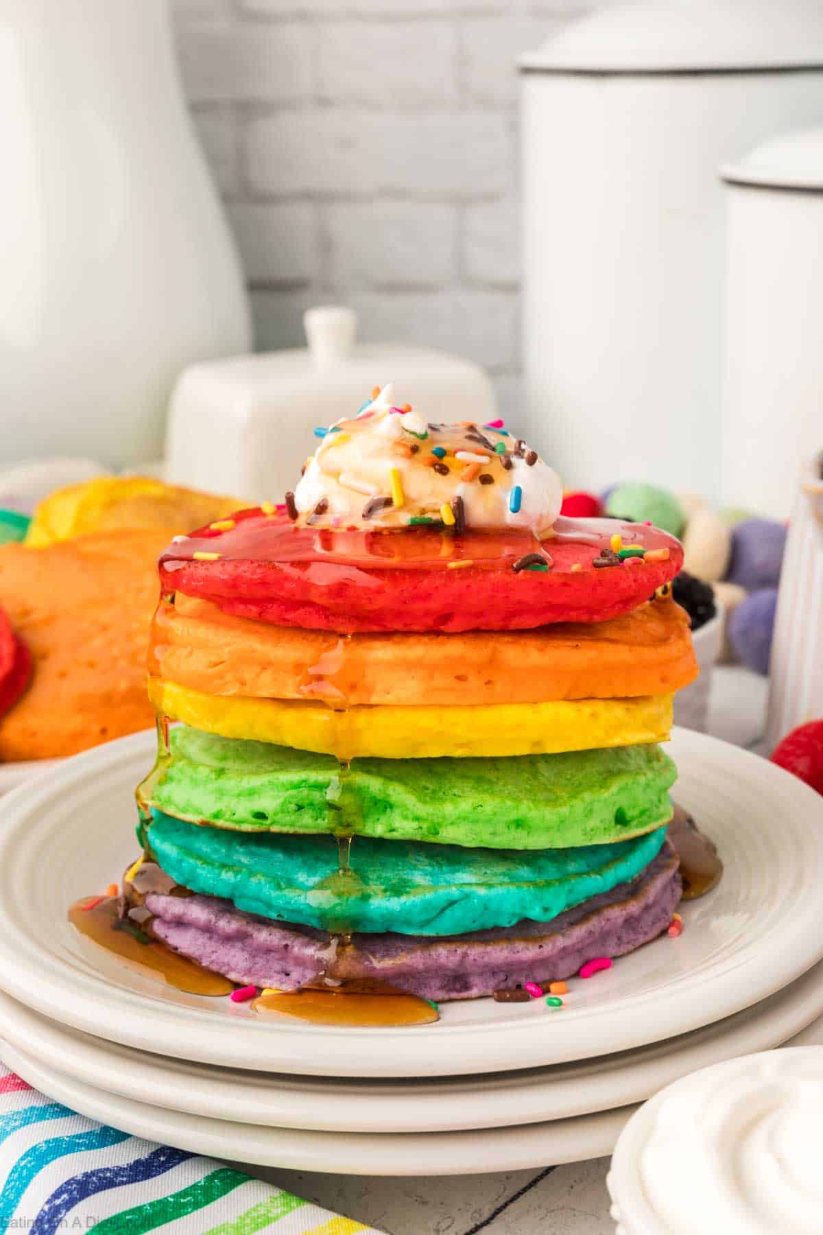 Rainbow Pancakes stacked topped with maple syrup and whipped cream