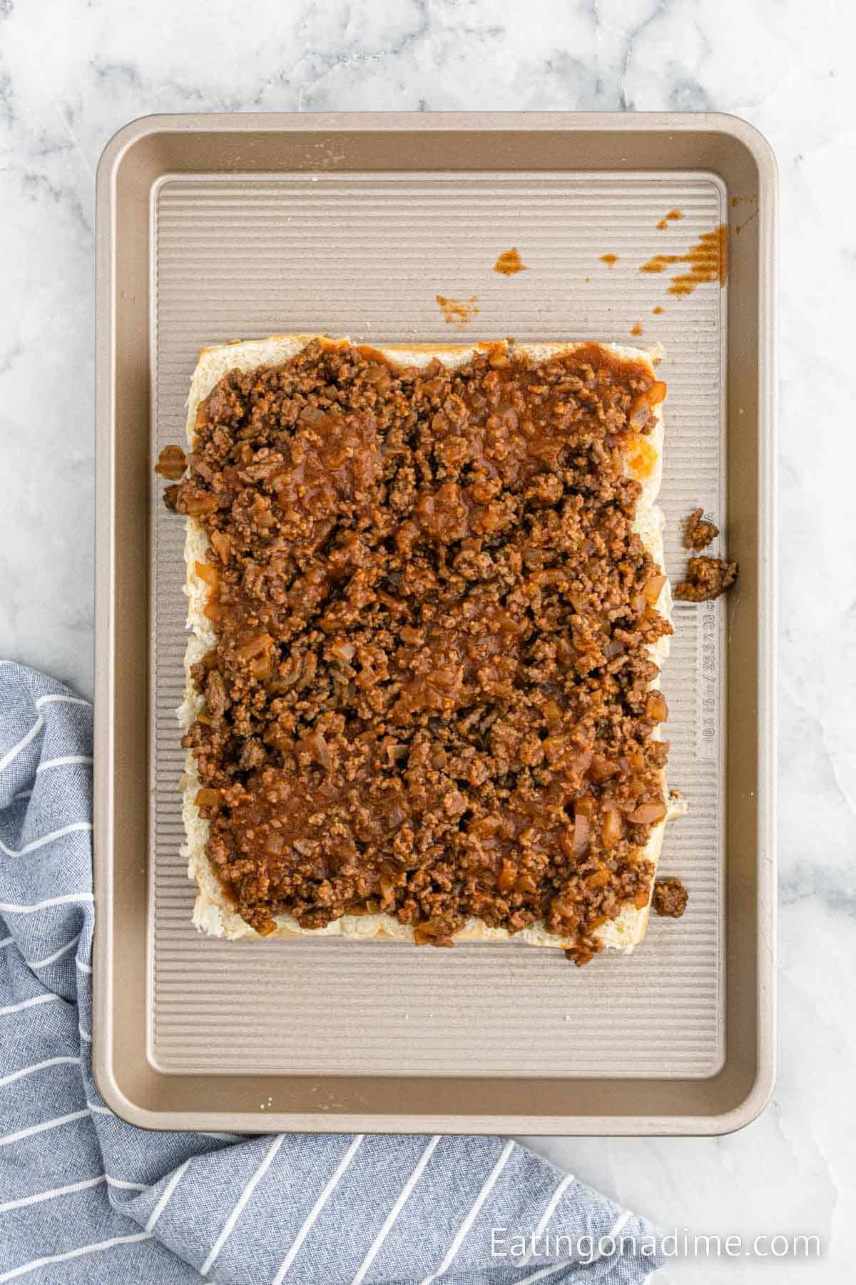 Spreading the beef mixture on the bottom rolls on a baking sheet