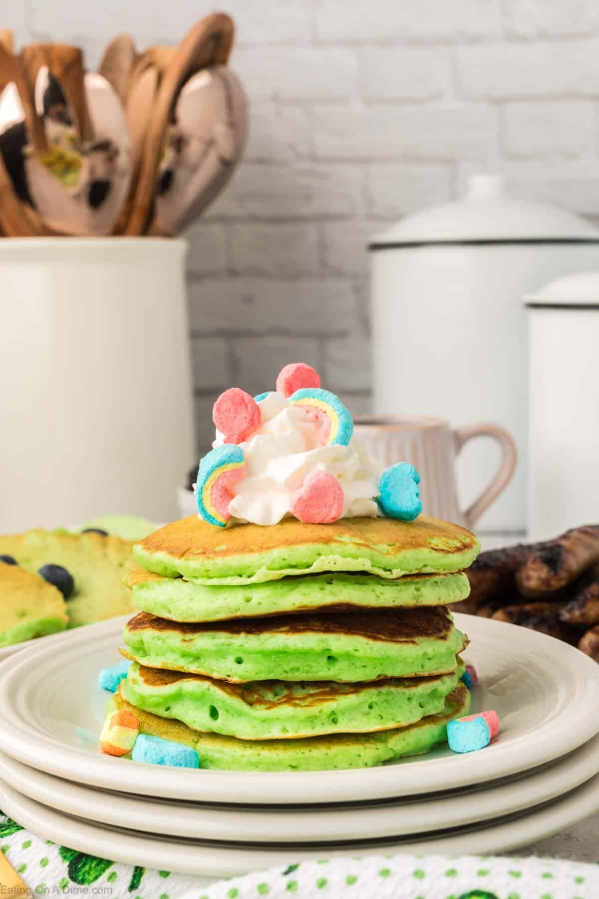 Green pancakes stacked on a plate topped with whipped cream and lucky charms 